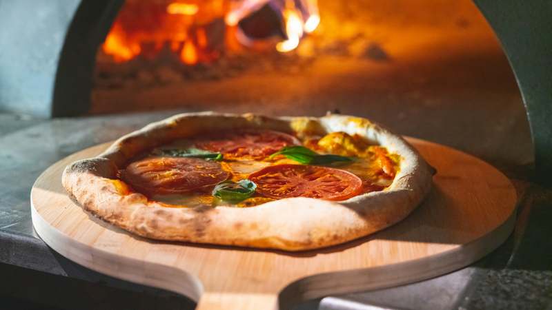 Modern kitchen with a countertop pizza maker, fresh ingredients, and a golden-brown artisan pizza on a wooden peel